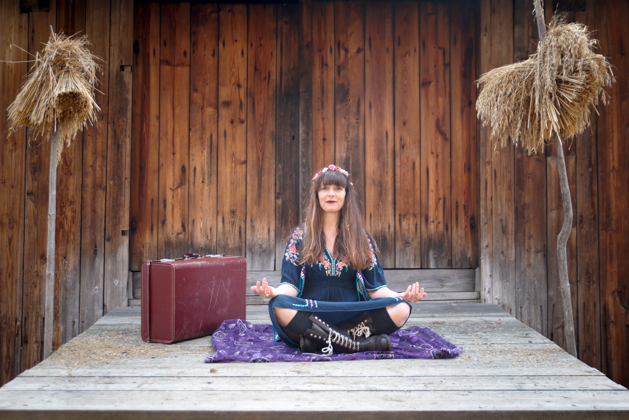 Kvinne sittende i meditasjonsstilling med koffert stående ved siden av :foto